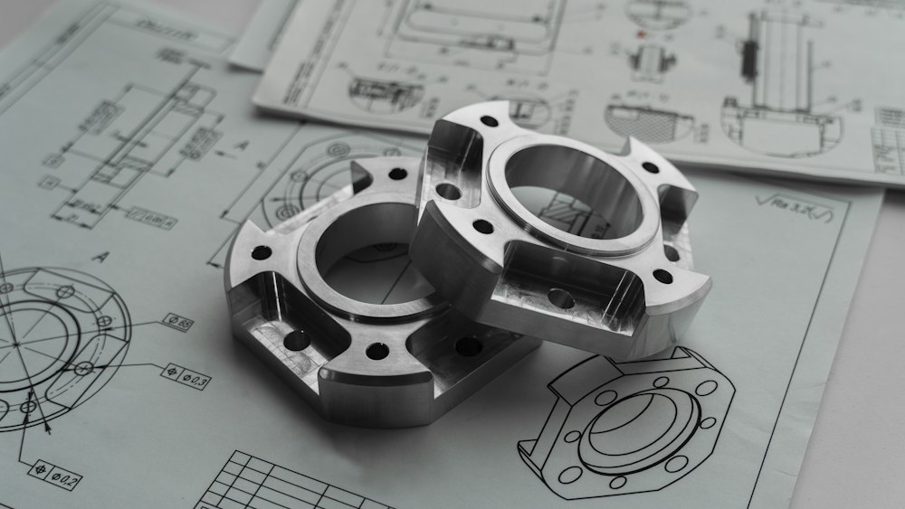 Machined aluminium prototype components resting on engineering drawings