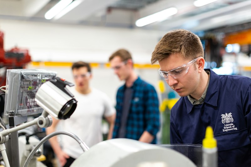 Students in safety glasses working with machinery in a college engineering workshop